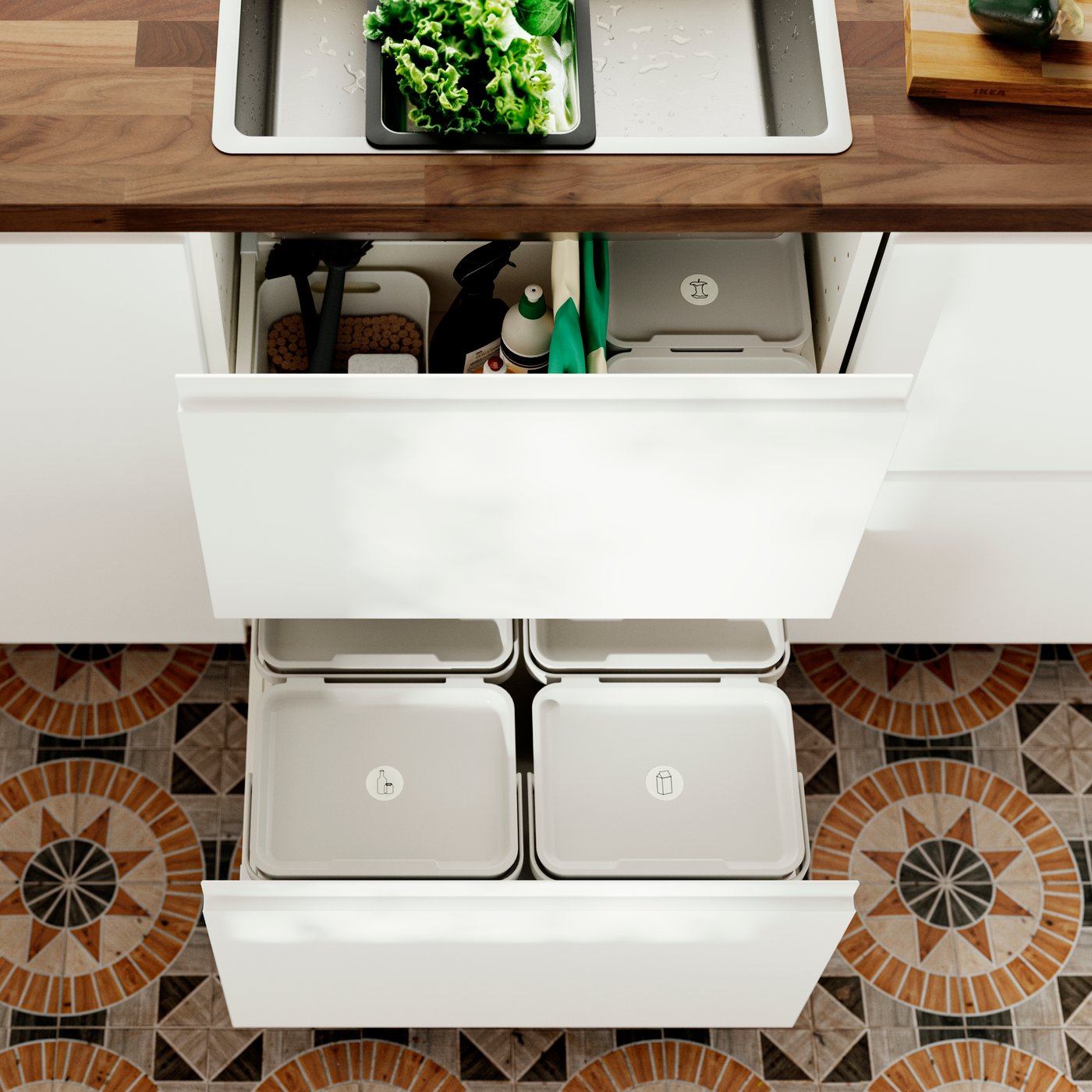 A close-up of multiple light grey HÅLLBAR bins with lids in a kitchen, beside cleaning supplies in drawers and a sink.