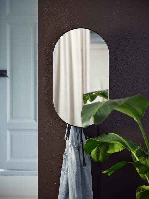 Bedroom wall has a rounded mirror with black frame, a hanging jacket, potted plant with green leaves, and a white door.
