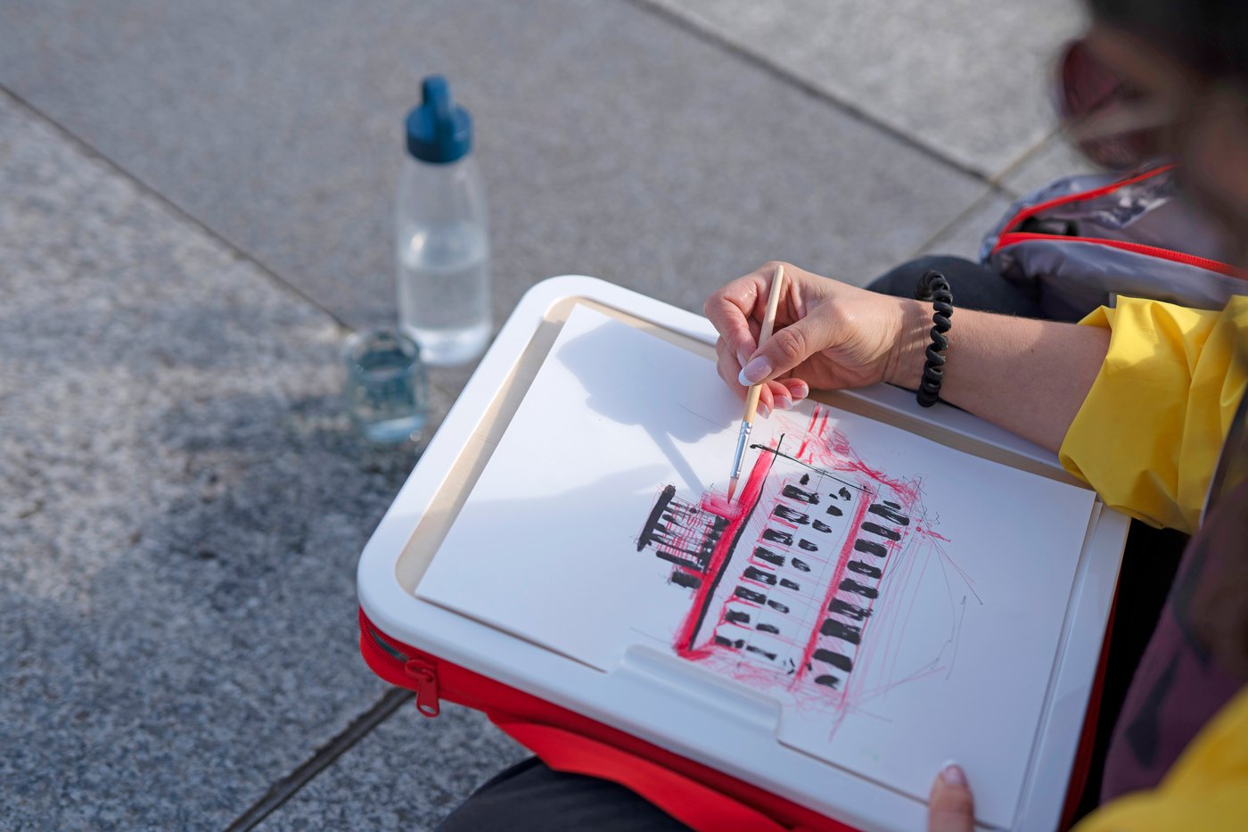 En person ritar på en portabel ritväska och i bakgrunden syns en vattenflaska.