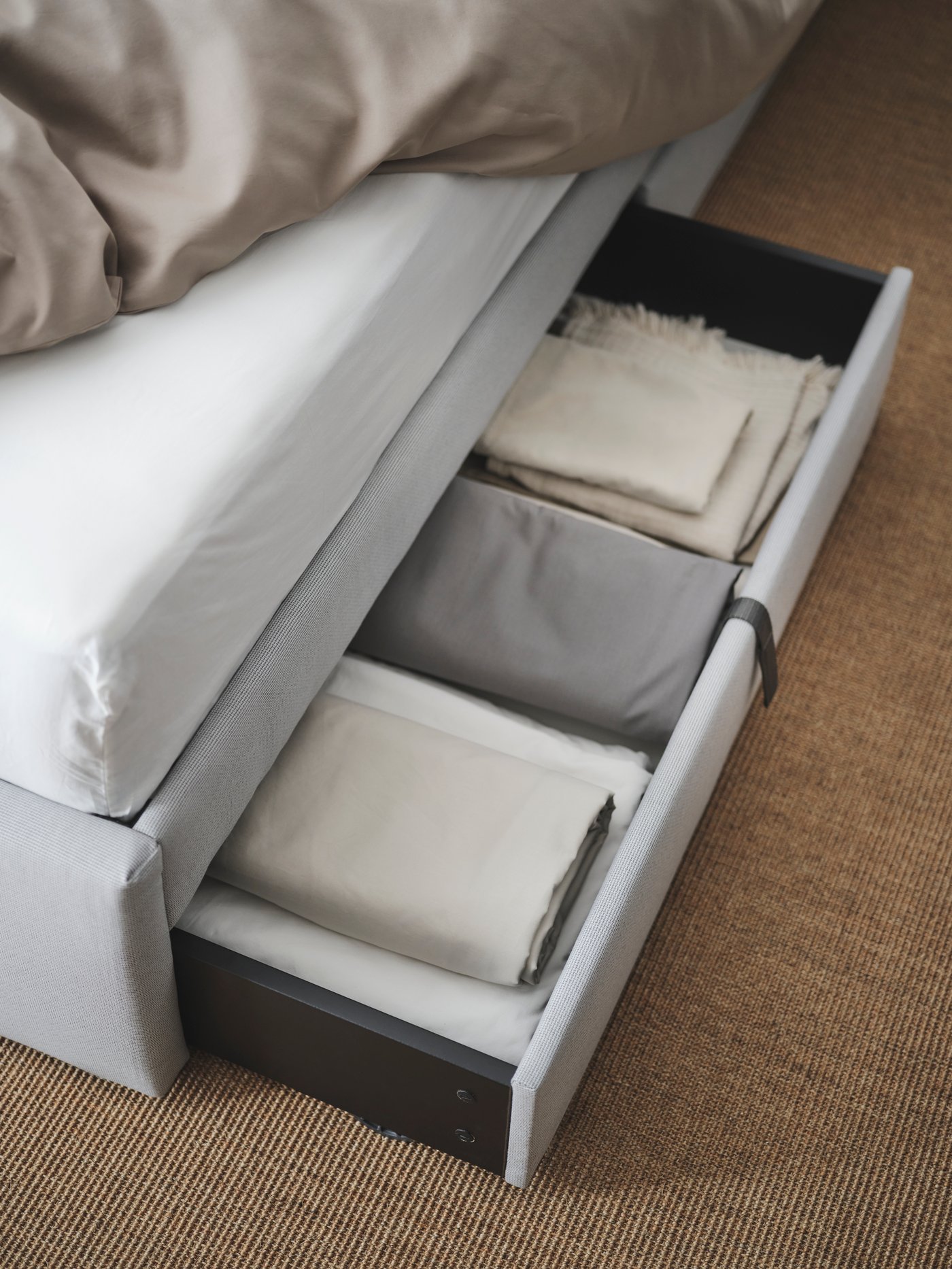 A GLADSTAD bed with two storage boxes underneath, one is pulled out and filled with bedlinen and extra blankets.