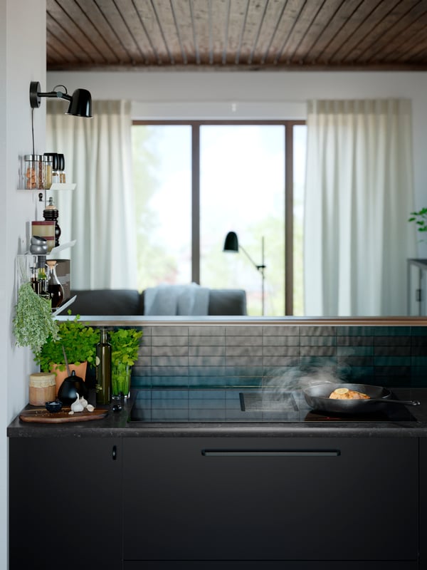 La nourriture est préparée dans une poêle à frire en fonte sur une table de cuisson à induction FÖRNEBO à côté d’un pot d’herbes et d’une bouteille d’huile.