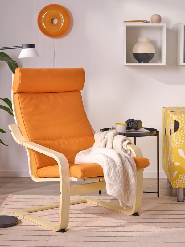 POÄNG armchair with an orange cushion in a bright living room with a yellow sofa.