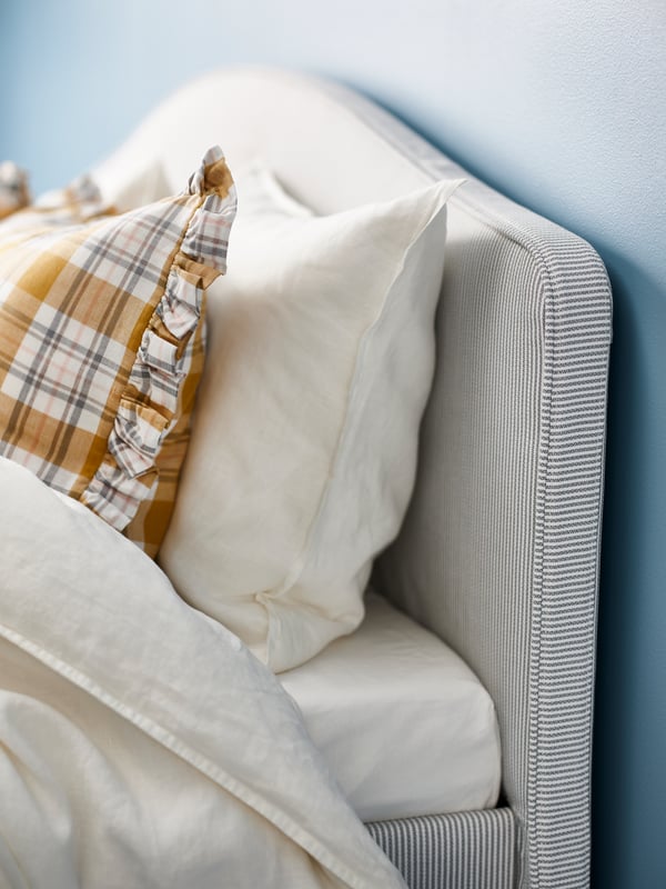 A patterned pillow and a plain white pillow are resting against the striped headboard of a RAMNEFJÄLL bed.