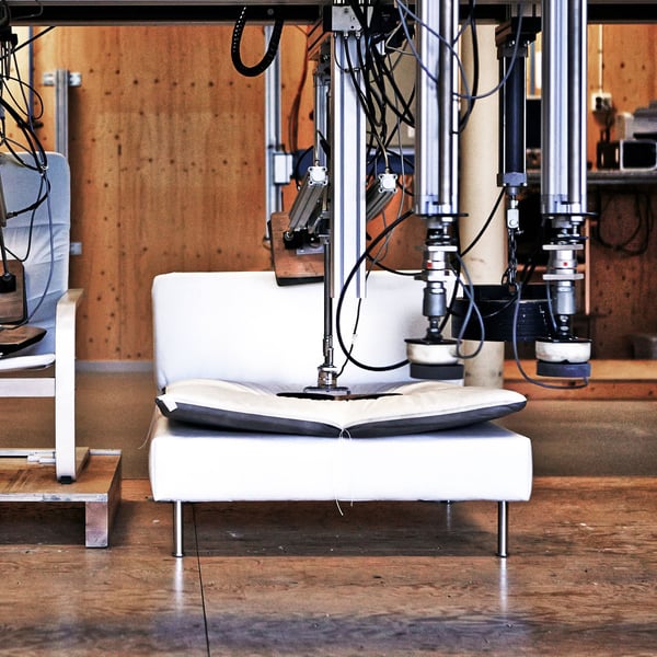 A white sofa undergoing a mechanical durability test with robotic equipment pressing on the cushions.