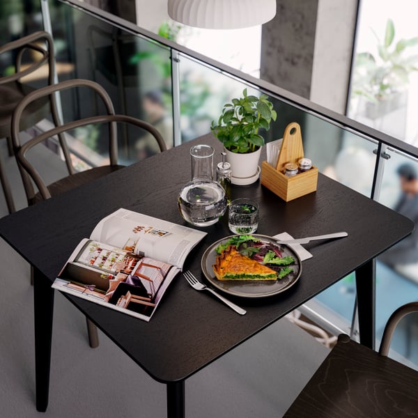 Close-up of a black LISABO table with food, water, CHOKLADHAJ table organiser and a magazine on top.
