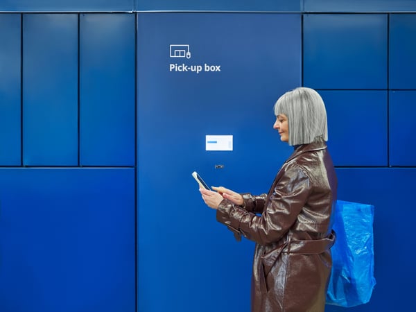 A customer is using her smartphone in front of a Pick-up box for Collect.