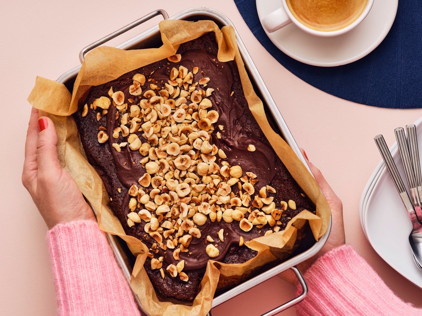 Hands holding a pan of brownies with toppings on it.