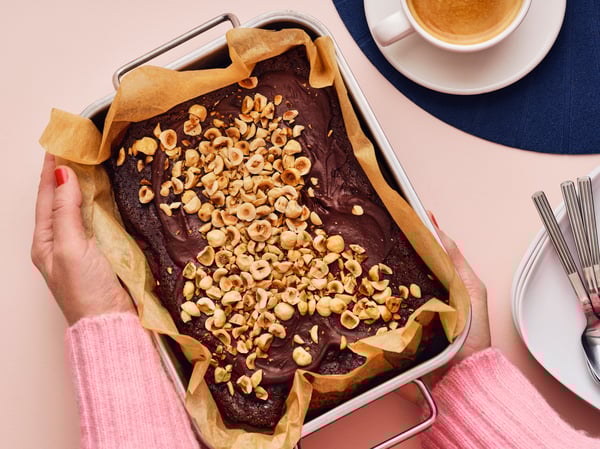 Hands holding a pan of brownies with toppings on it.