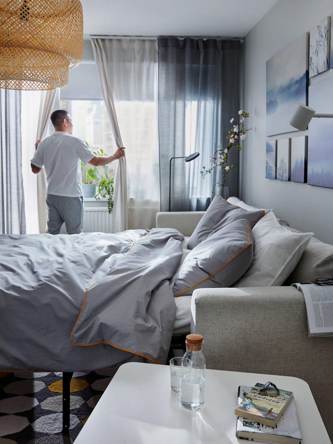 Man som håller på att dra för en tunn gardin i ett stort vardagsrumsfönster,.