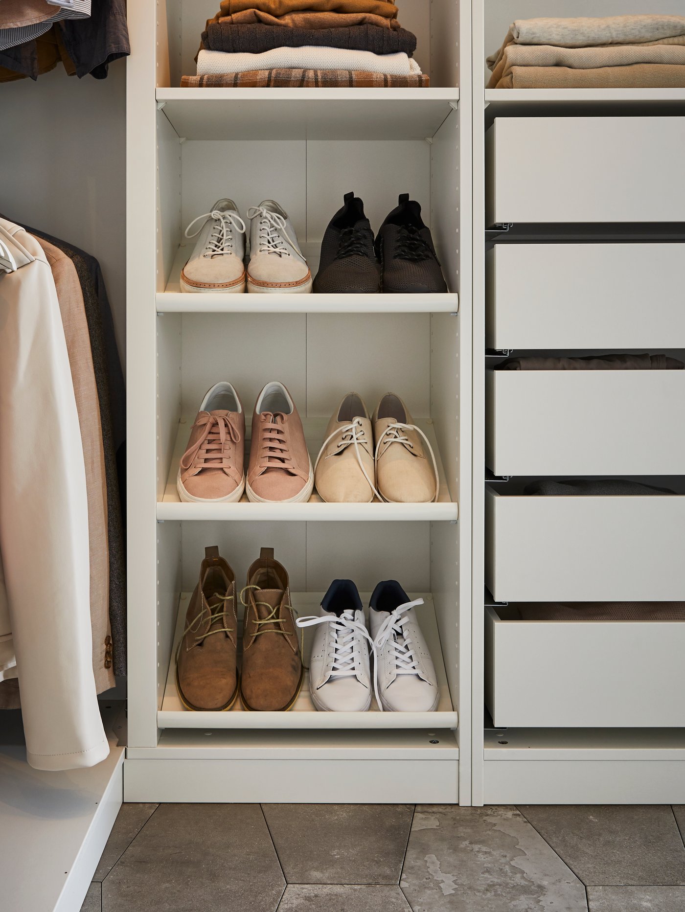 Parte inferior de un armario abierto con estantes y cajones junto a tres estantes blancos para zapatos KOMPLEMENT con varias zapatillas.