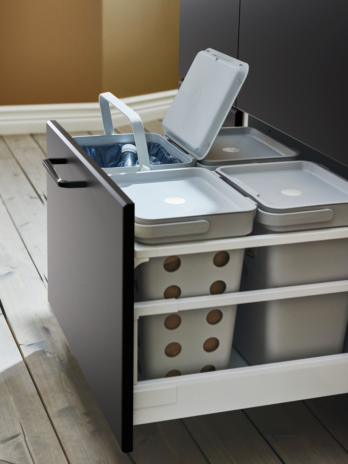 Un cajón de cocina profundo y extraído que revela una solución completa de cuatro botes de basura ventilados HÅLLBAR de color gris.