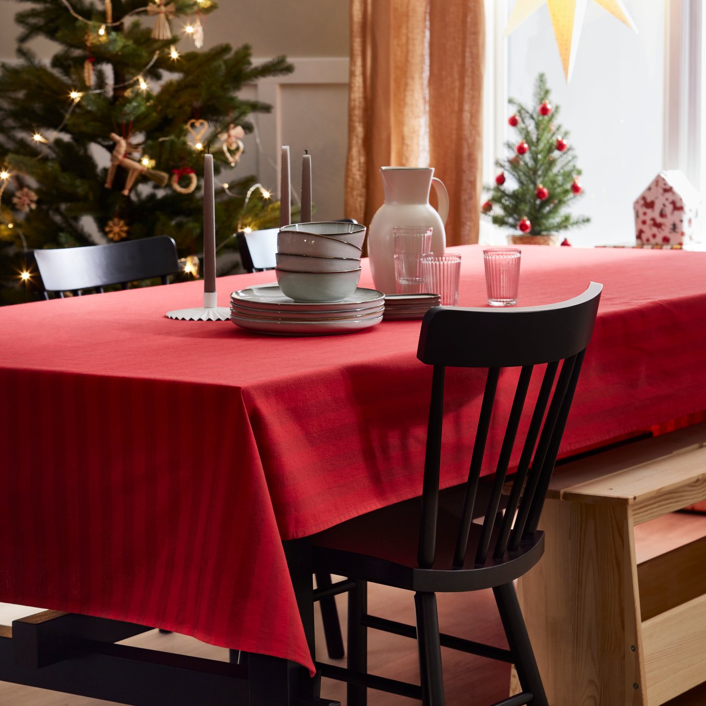 Una mesa con mantel navideño rojo y vajilla arrumbada una sobre otra. Detrás de la mesa hay un árbol de navidad.
