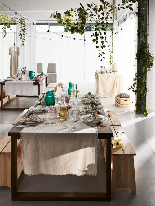 A festive table laid for a formal occasion with a bench for guests to sit placed in a light open space with other tables.
