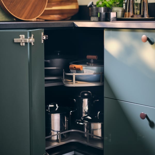 Une porte escamotable s'ouvre pour présenter un carrousel de base d'angle UTRUSTA contenant diverses casseroles et poêles, ainsi que des protège-casseroles BEDÖMA.
