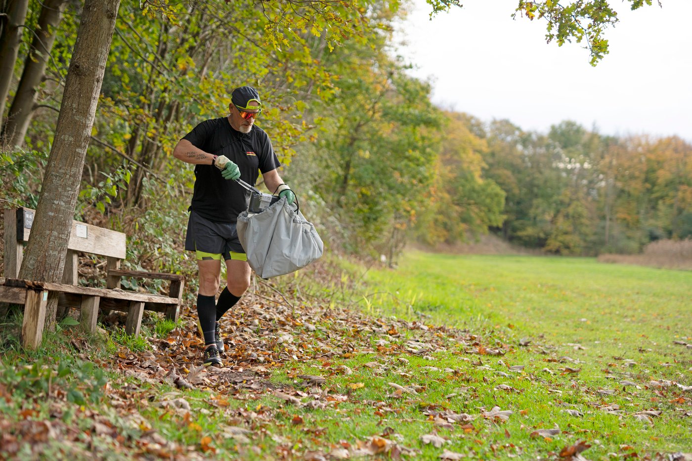 A man jogging in the nature while picking up trash and putting it in a AJÖSS waste bag.