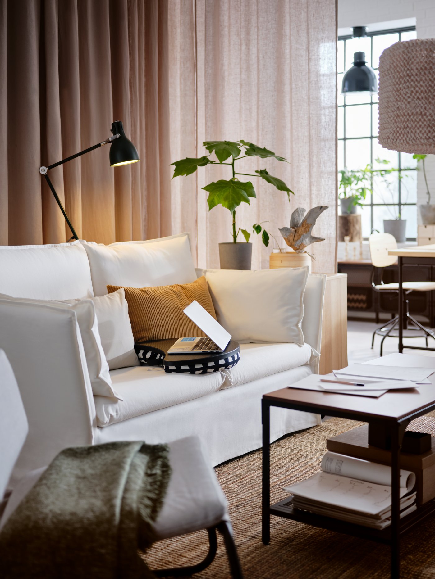 A white sofa, a potted plant, a laptop on a black/white laptop support, a black coffee table.