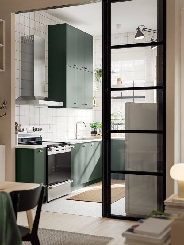 A wide doorway into a kitchen with deep green HAVSTORP kitchen fronts and a white marble effect/laminate EKBACKEN worktop.