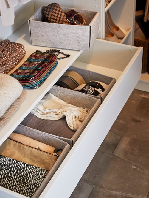The bottom of a wardrobe interior has an open drawer with a row of light grey KOMPLEMENT boxes holding groups of accessories.