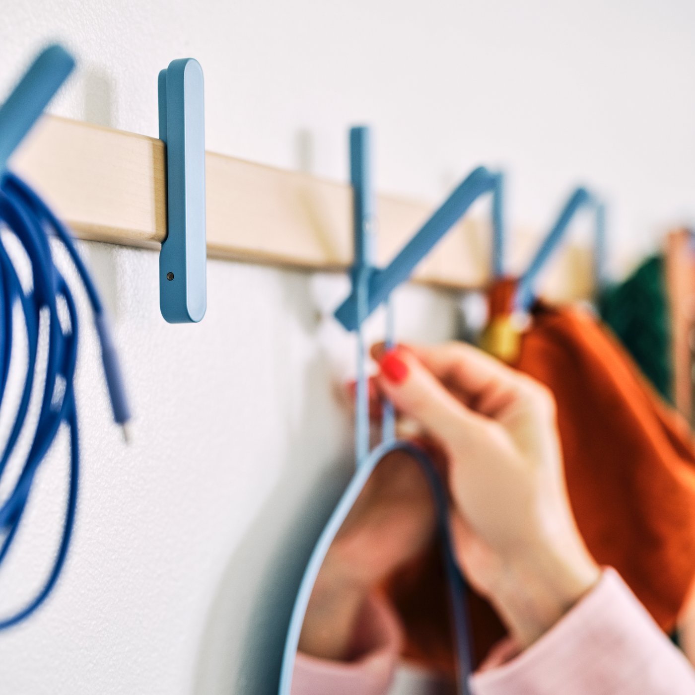A person hangs something on one of the automatically retractable hooks of an IKEA PS 2026 rack with 5 hooks.