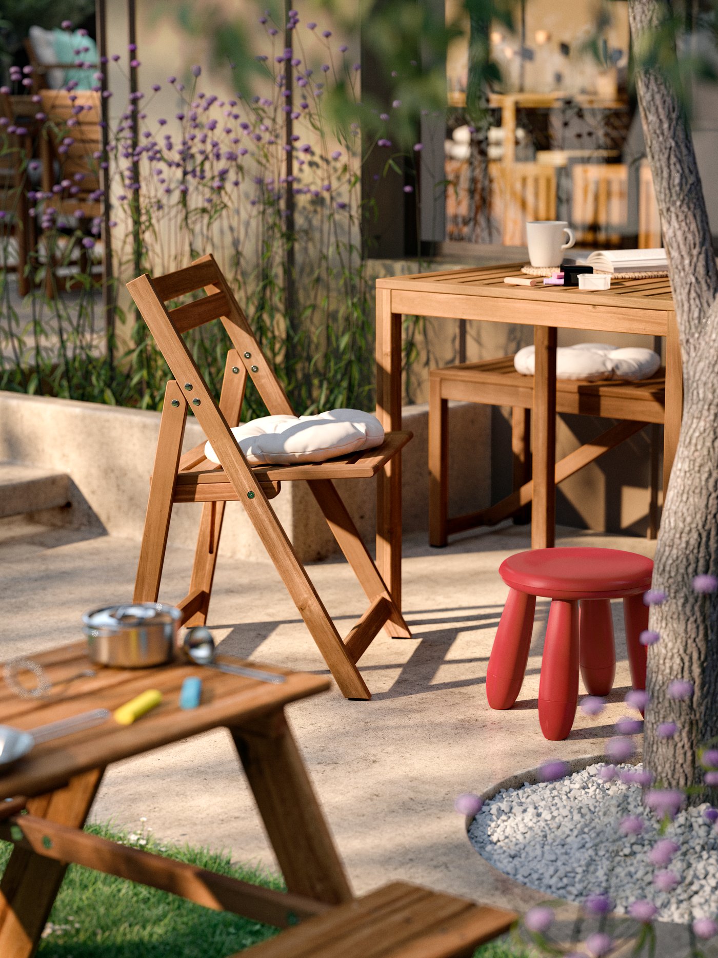 A patio corner with a RESÖ children’s picnic table and a red in/outdoor MAMMUT children’s stool next to NÄMMARÖ furniture.