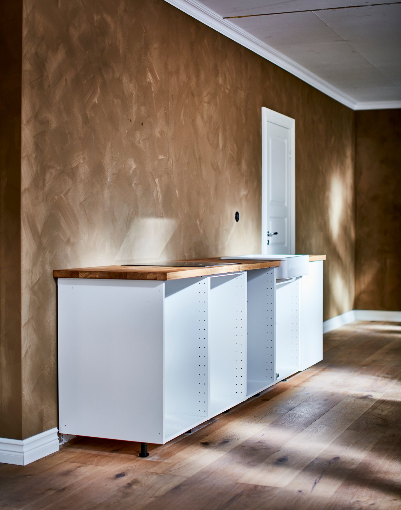 Ein weisser METOD Unterschrank ohne Türen vor einer in einem tiefen Braunton gestrichenen Wand.