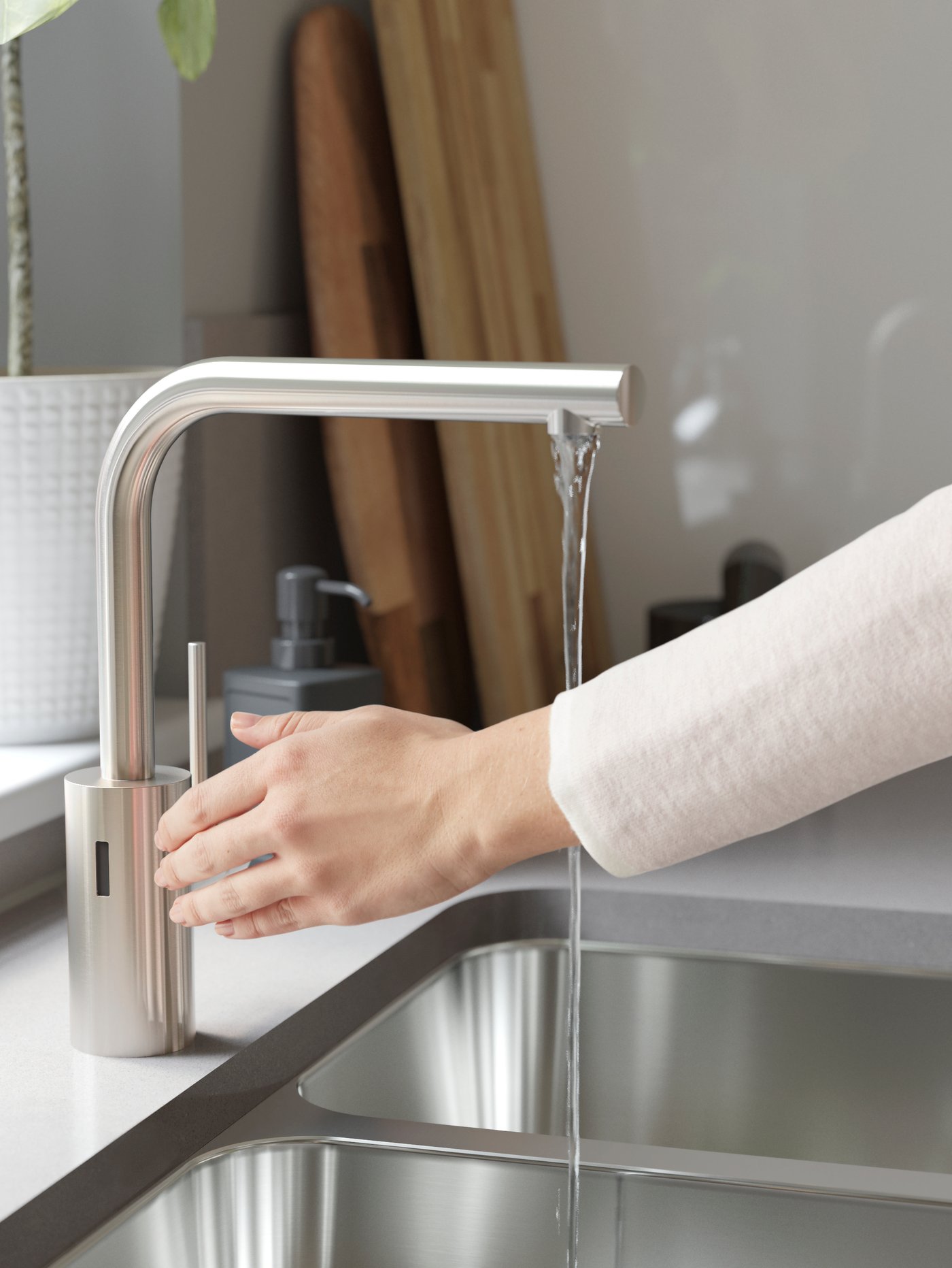 A person with a white top activates the IKEA TÄMNAREN motion sensor stainless steel sink tap, turning on the water.