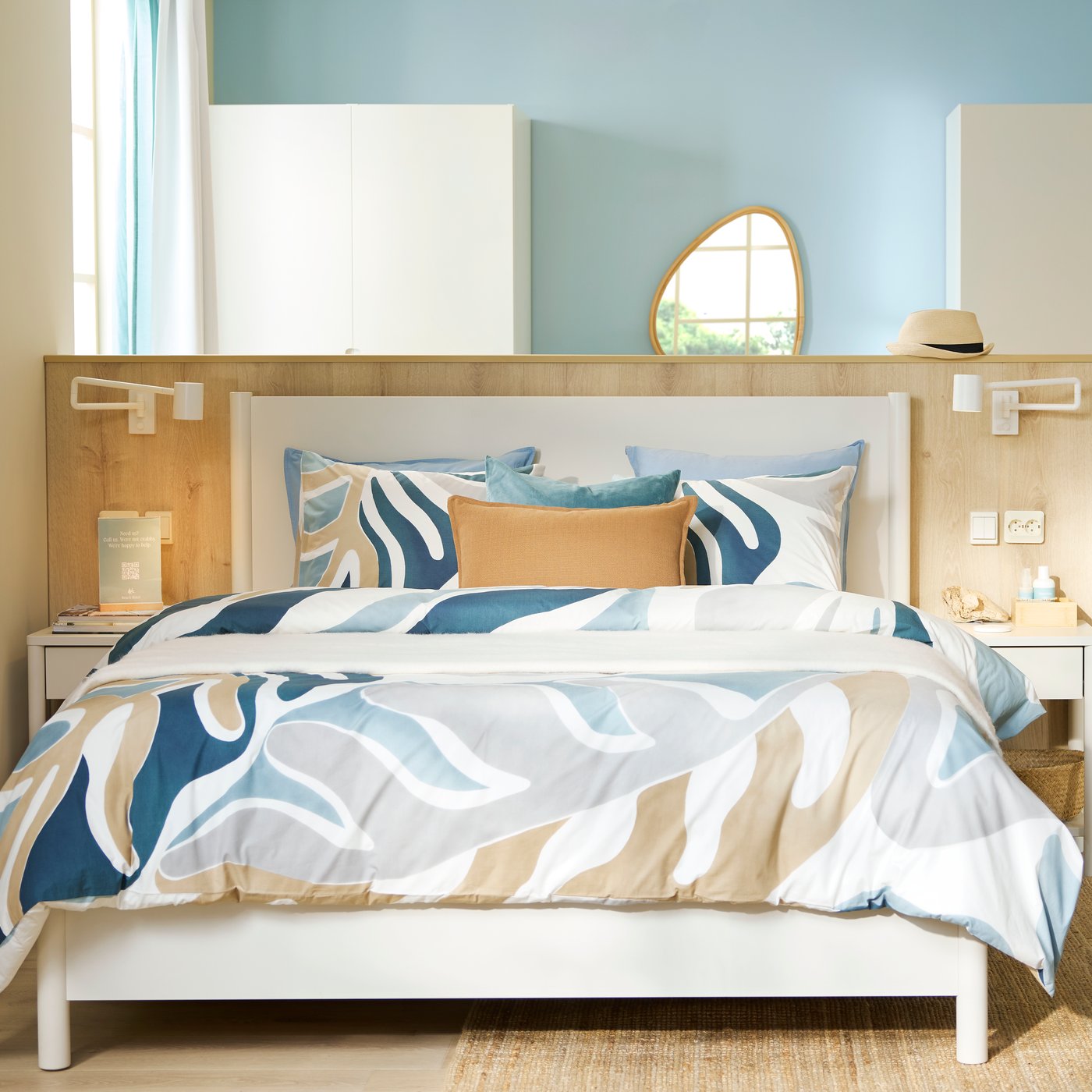 An airy, beachy-feeling hotel room has beige and light teal walls with an off-white TONSTAD bed frame in the room’s centre.