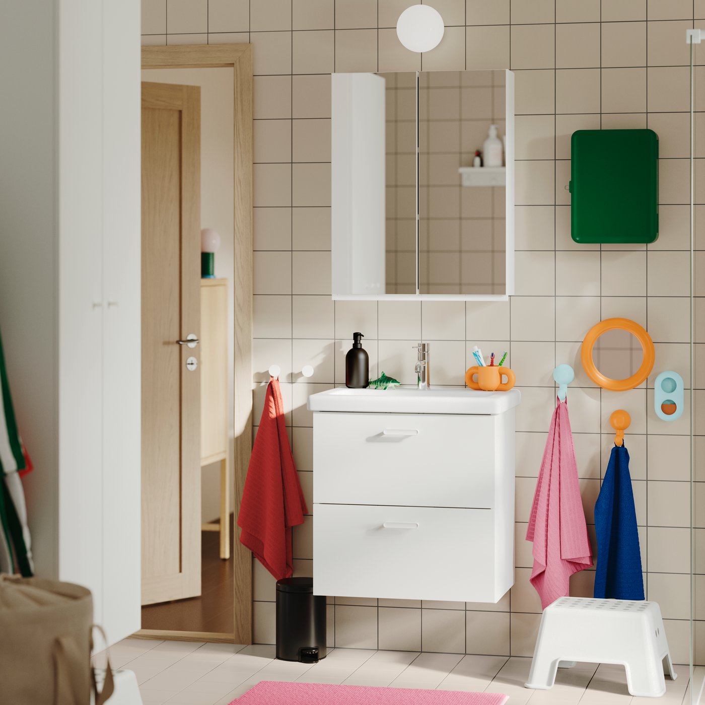 A tiled bathroom featuring the white TVÄLLEN/ENHET wash-stand with two drawers, wall-mounted with colourful towels nearby.