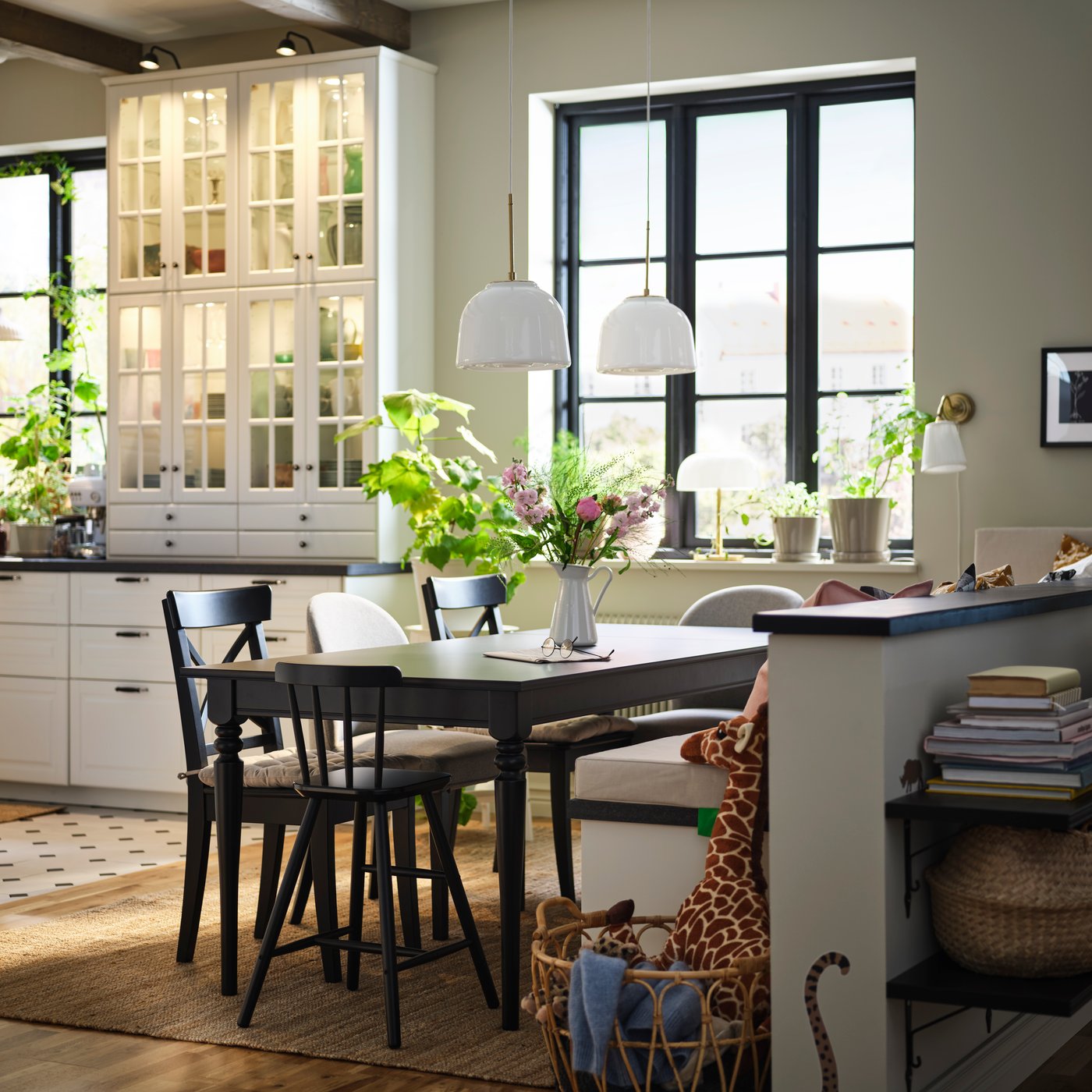 A dining area with ROSENTORP black wooden table and chairs, styled with flowers in a vase, next to a basket with soft toys.