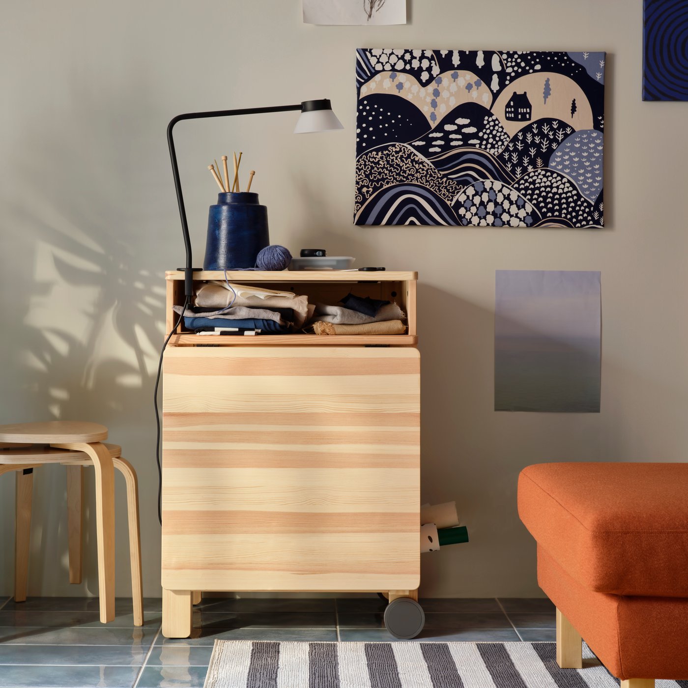 A sunlit living room with a pine RESARÖ mobile drop-leaf table in folded mode, by a wall and next to stacked KYRRE stools.