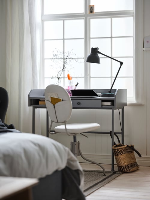Home office area with rectangular grey desk with hidden storage area with sliding front, white chair, and work lamp.