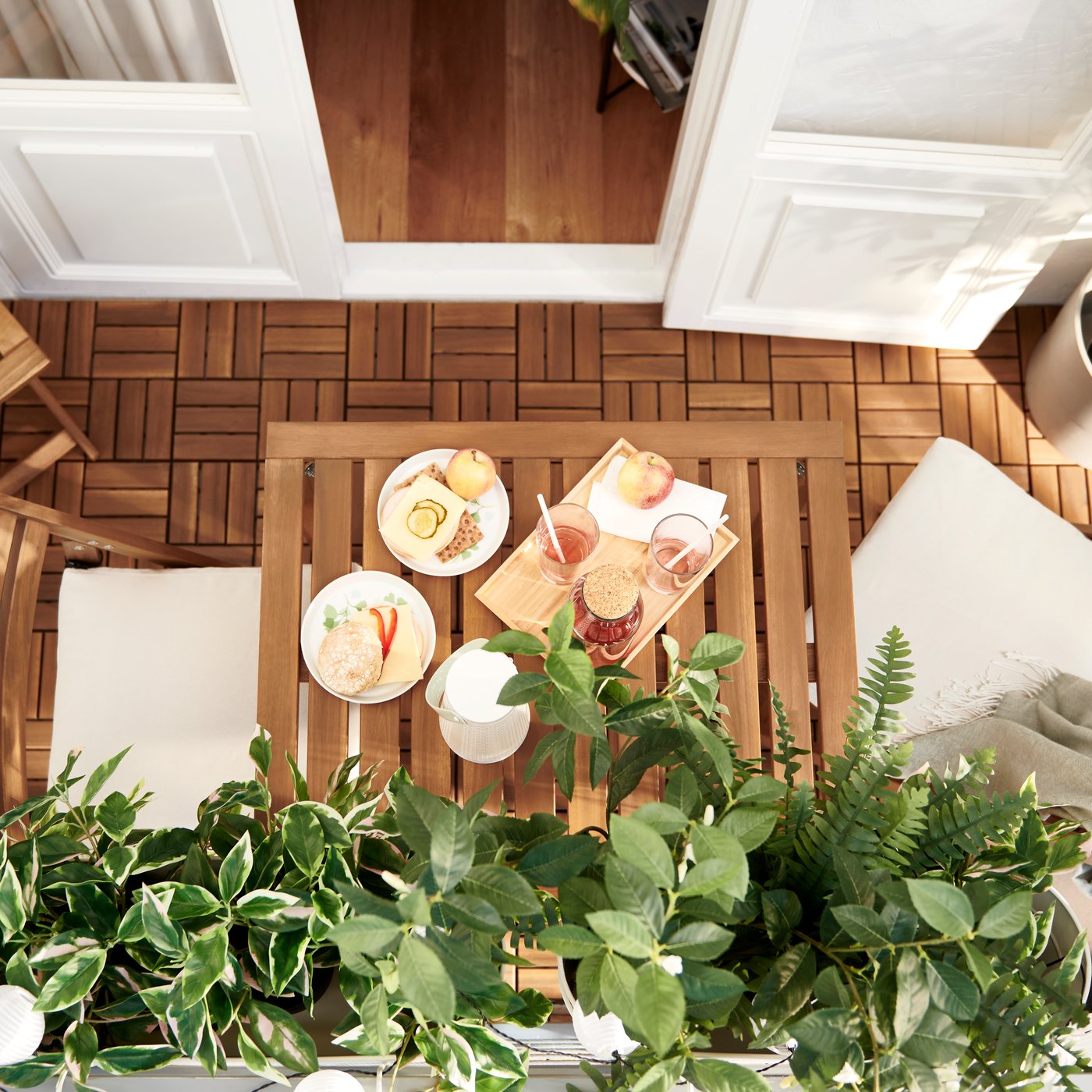 Un balcone arredato con piante artificiali FEJKA verdi e mobili NÄMMARÖ e pedana per pavimento RUNNEN in doghe di acacia.