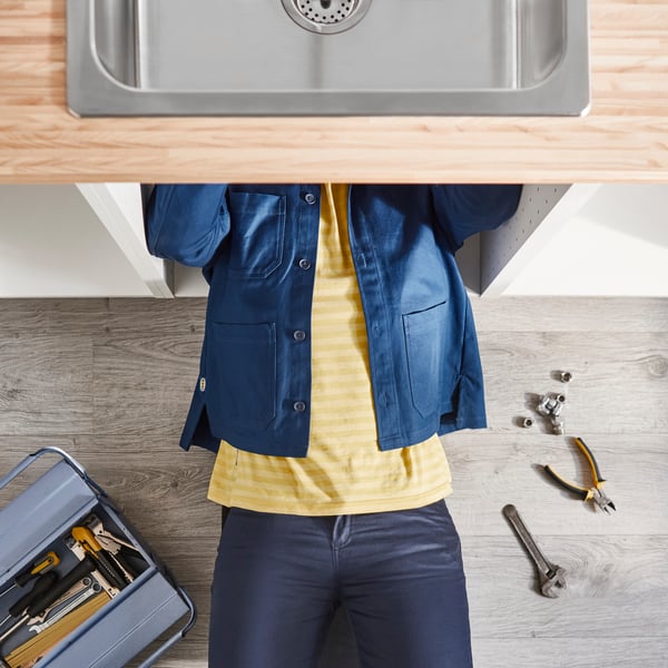 A professional IKEA installer working on the pipes of a sink in an IKEA kitchen.