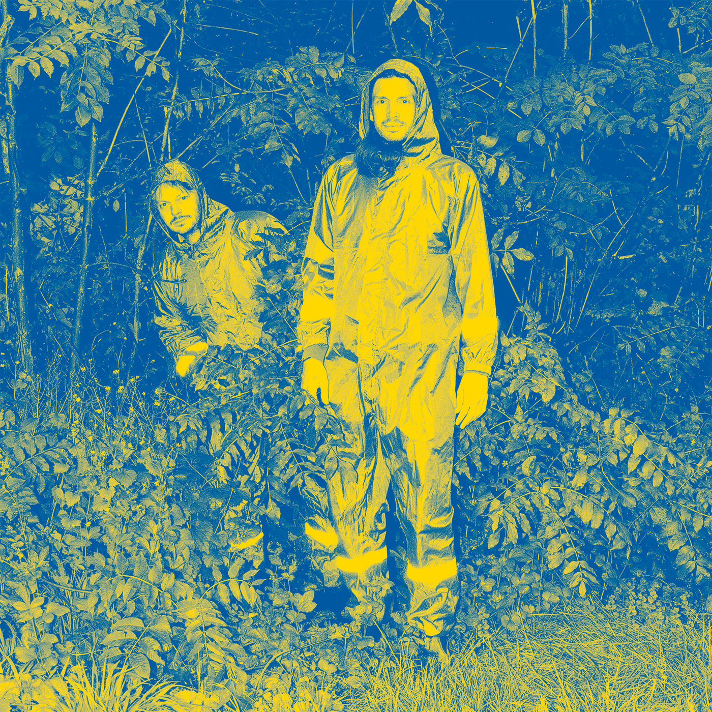 Due persone di Public Possession in piedi in un bosco con indosso una tuta da lavoro.