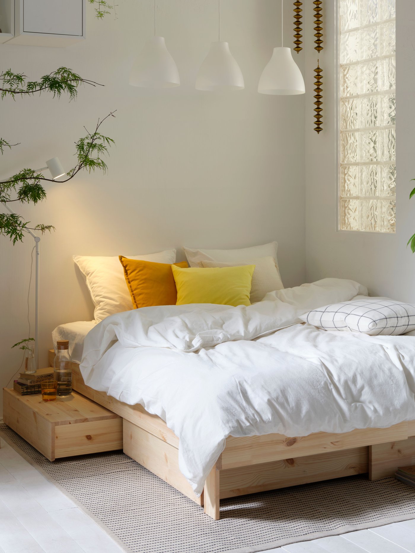 A GLAMBERGET bed with storage is tucked in a corner of a bedroom. ÄNGSLILJA bedding and SANELA cushions are on the bed.