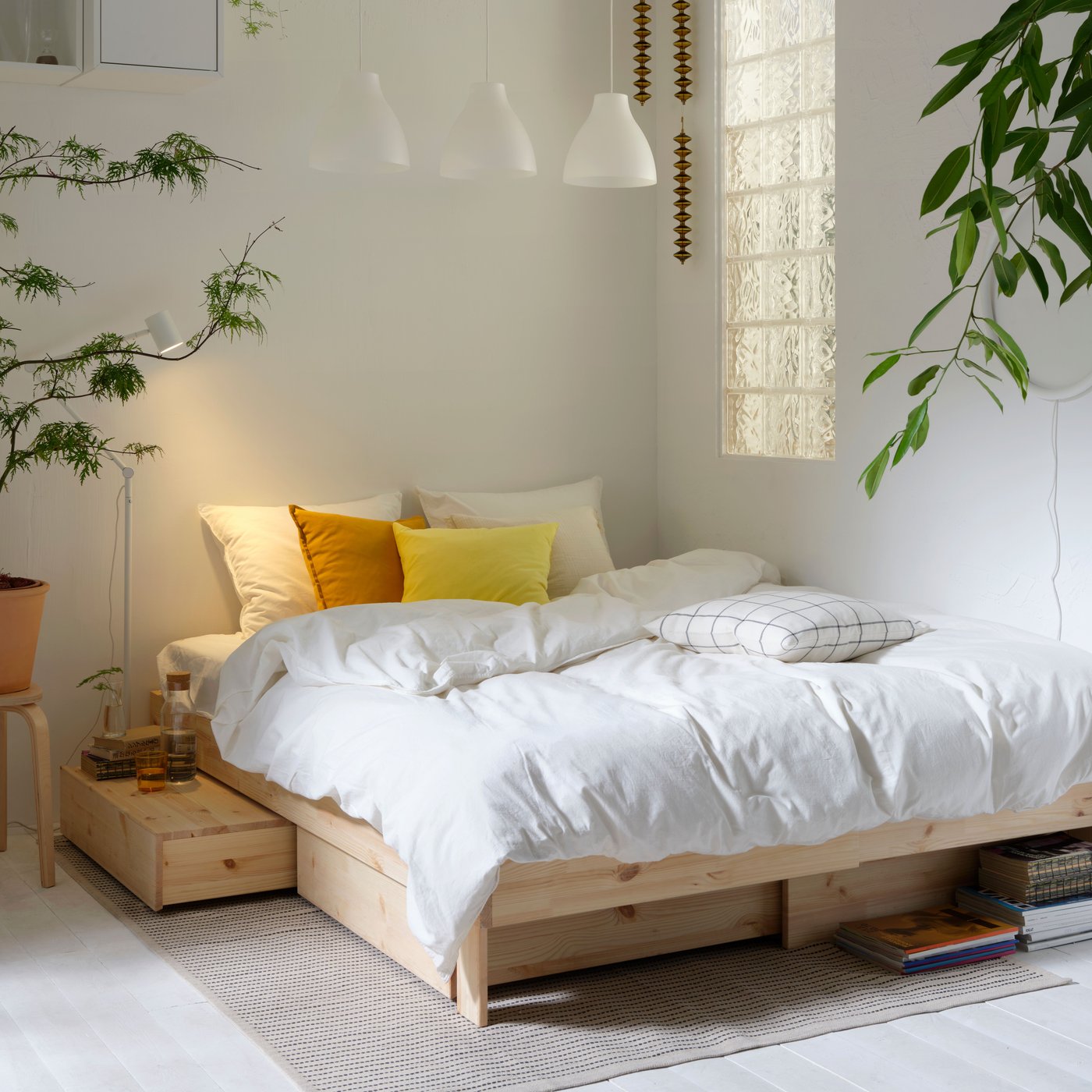 A GLAMBERGET bed with storage is tucked in a corner of a bedroom. ÄNGSLILJA bedding and SANELA cushions are on the bed.