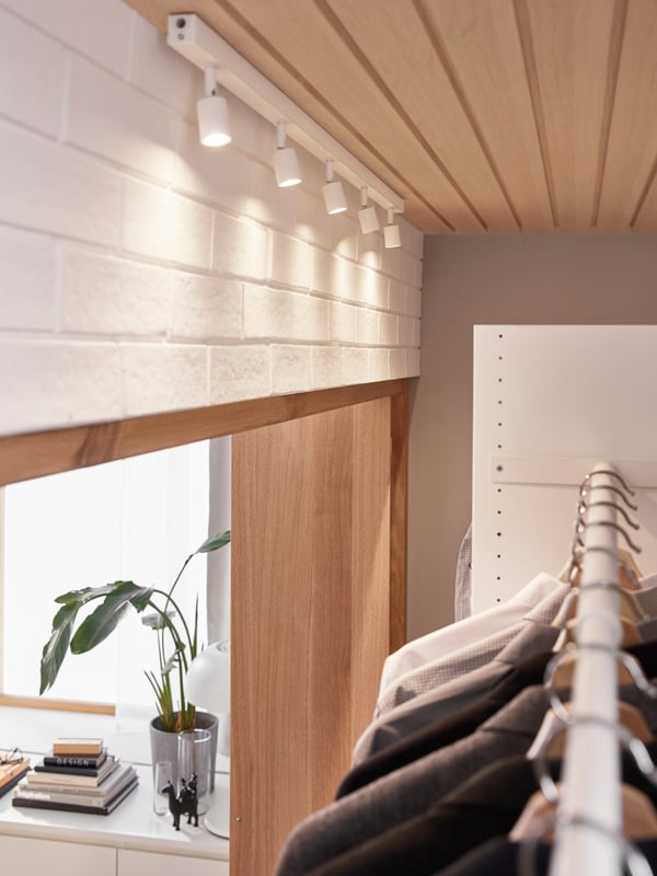 A white BÄVE LED ceiling track with adjustable spotlights shines on the clothes hanging inside a fitted AURDAL wardrobe.