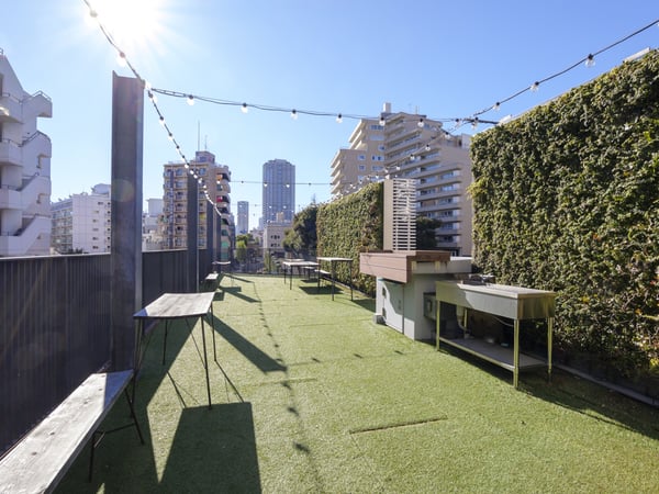 人工芝が敷かれた屋上スペース。ベンチとテーブルが並び、上空にはストリングライト