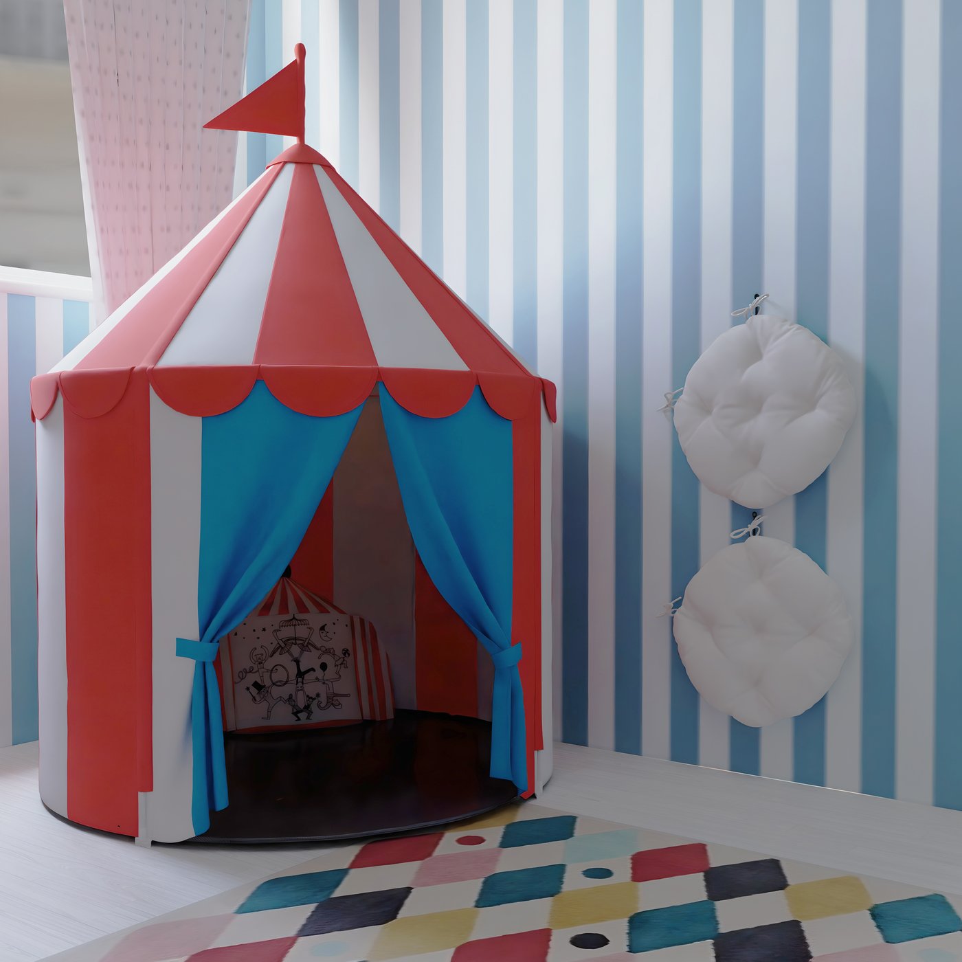 Carpa de circo CIRKUSTÄLT, en su interior hay un cojín BUSENKEL. Colgados en dos percheros de pared hay dos cojines KUDDARNA blancos y en suelo hay una alfombra BUSENKEL de rombos multicolor.