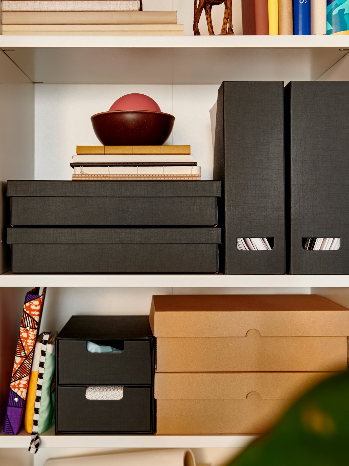 An anthracite FJÄDERHARV magazine file on a shelf, alongside decorative boxes and books in a well-organised space.
