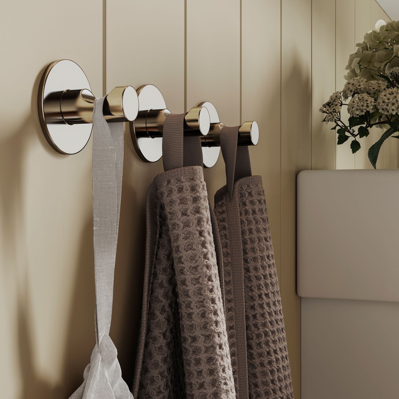 Deux serviettes sont suspendues à des crochets autocollants SKOGHALL placés sur un mur gris-vert à côté d’une armoire blanche.