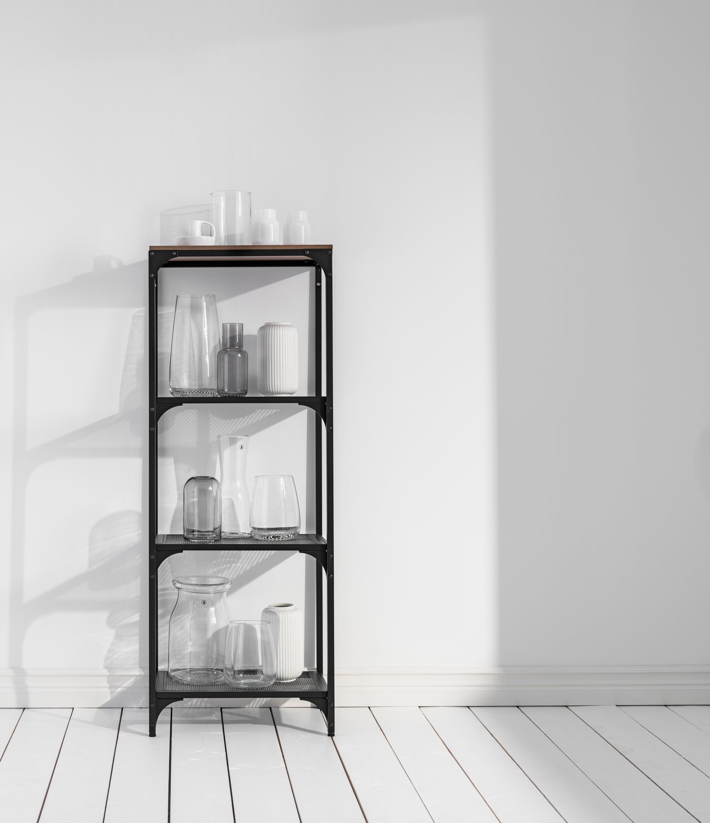 Uno scaffale nero con appoggiati sui ripiani diversi vasi in vetro e ceramica