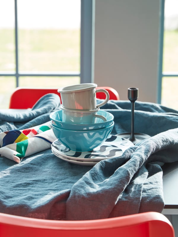 A breakfast table setting for two with a table cloth, mugs, tableware and turquoise FÄRGRIK bowls.