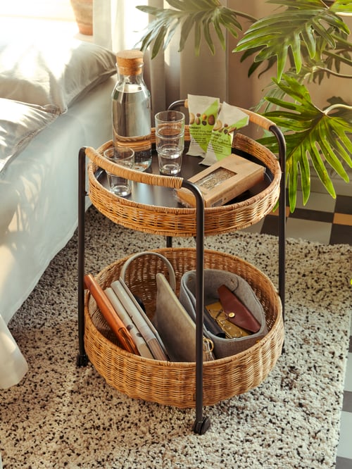 Living room featuring a rattan trolley table with storage containing a carafe with stopper, glasses, books, and a basket. 