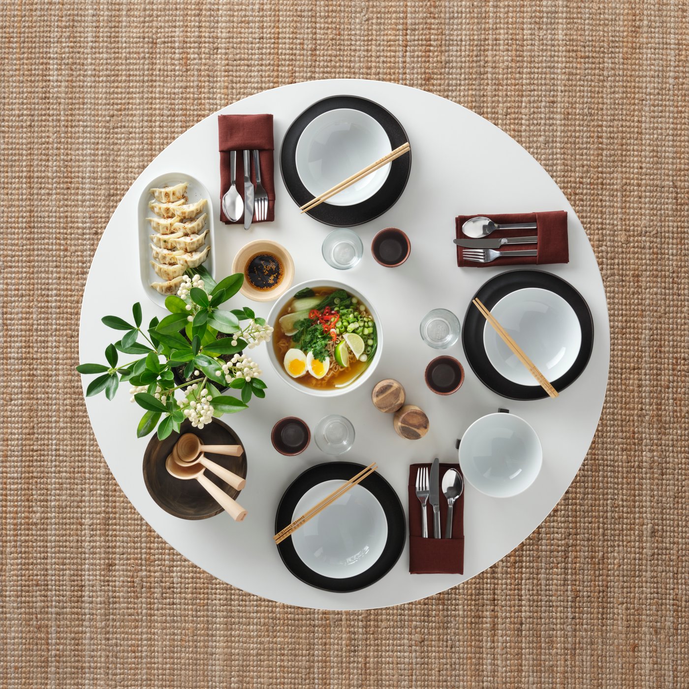 A round table set for a meal with food, IKEA 365+ deep plates, a set of 3 FLODNEJONÖGA wooden spoons and IKEA 365+ cutlery.