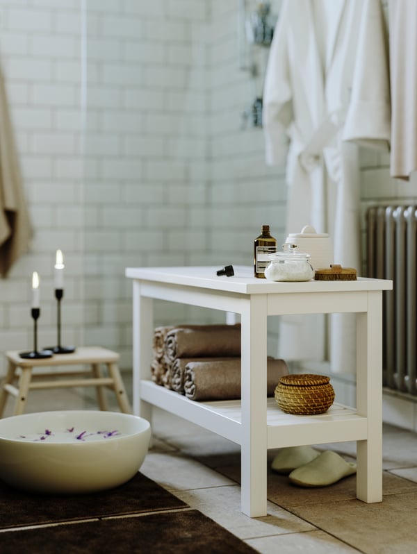 Weiße Sitzbank aus Holz im Badezimmer, bestückt mit Badaccessoires.