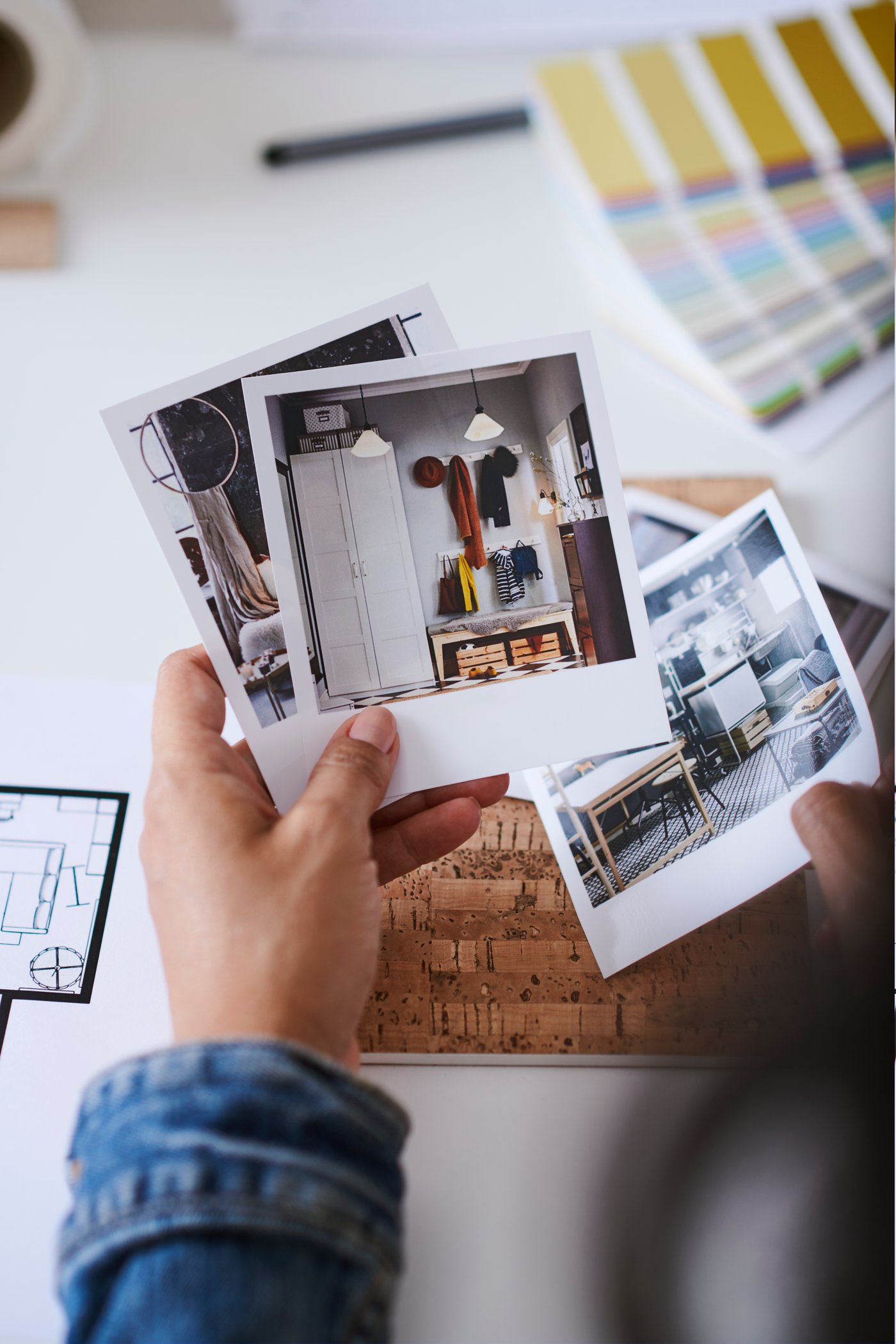 Een hand houdt een aantal inspirerende polaroids vast met beelden van verschillende interieurs. Op de achtergrond ligt tekenmateriaal en een kleurenwaaier.