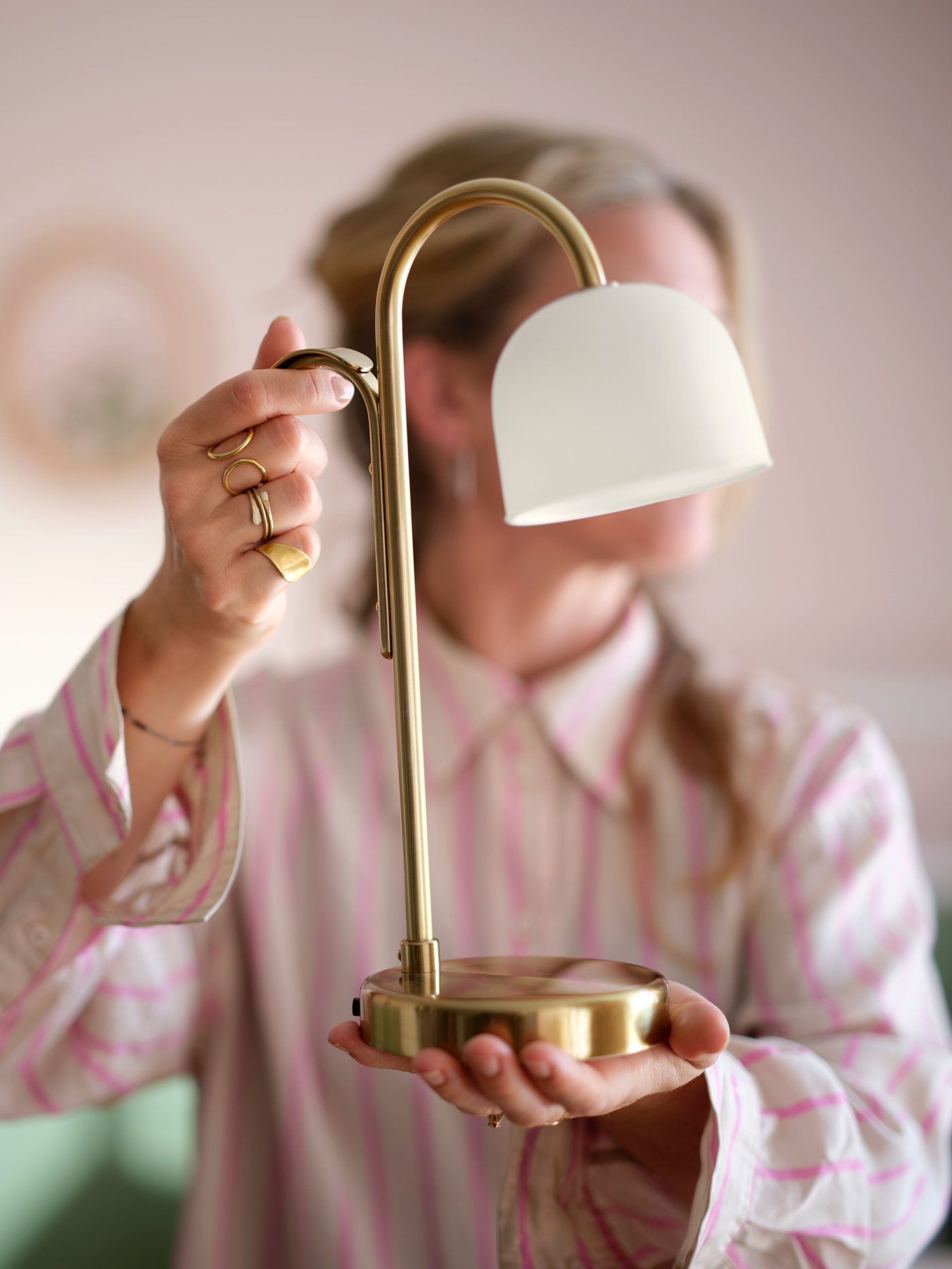 Person hält eine moderne Tischlampe mit goldenem Gestell und weißem Lampenschirm.