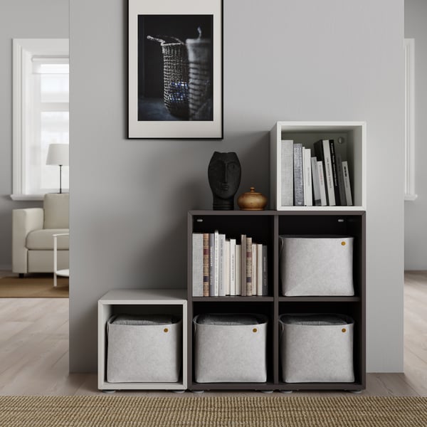 Planificador EKET color gris oscuro con decoración y libros encima, gabinetes de diferentes colores en la pared con accesorios en su interior.