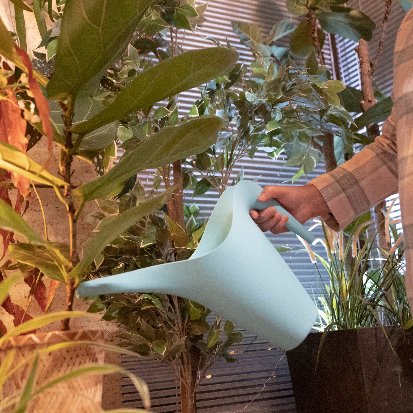 A woman in pyjamas is watering plants with a watering can.